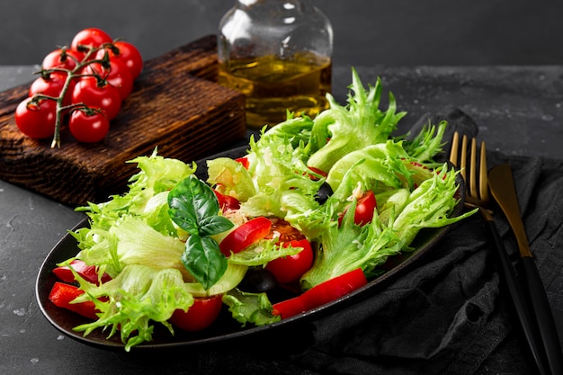 Ensalada de verano simple de tomates lechuga con aceitunas y aceite de oliva en una placa negra closeup