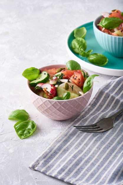 Foto ensalada de verano de verduras frescas con albahaca servido en un tazón. un tomate. pepinos, cebollas, rábanos. semillas de sésamo y semillas de calabaza