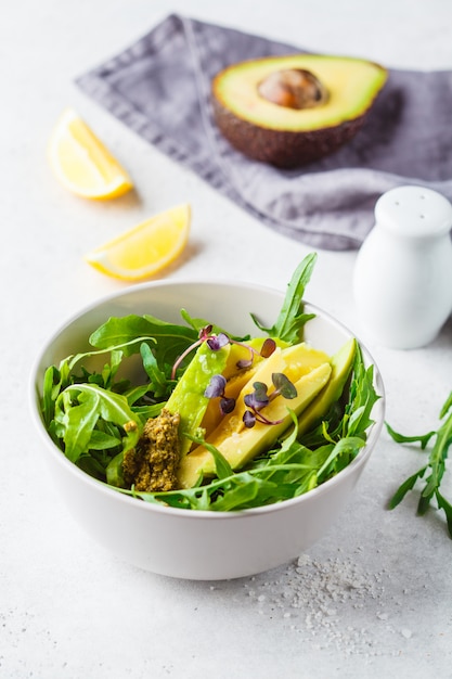 Ensalada verde del aguacate con arugula y pesto en cuenco gris. Concepto de comida vegana saludable.