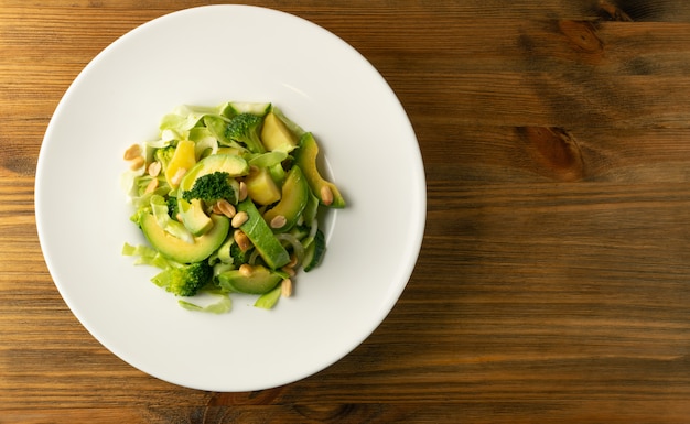 Ensalada verde con aguacate, pepino y nueces en plato blanco