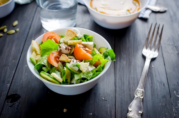 Ensalada verde clara fresca con pepino, lechuga, aguacate, tomates, sobre una mesa de madera oscura. Concepto de estilo de vida de alimentos saludables.