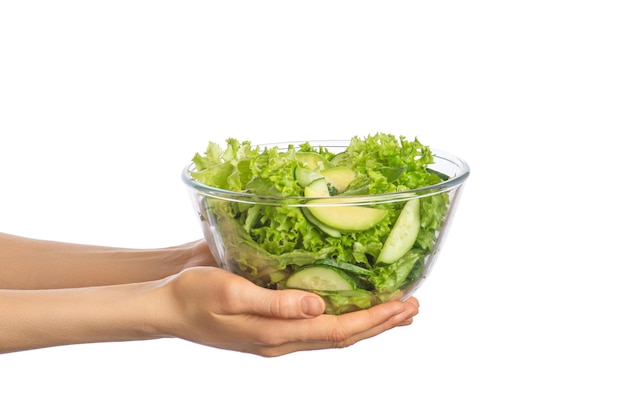 Ensalada verde en una ensaladera transparente en manos femeninas sobre un fondo blanco aislado