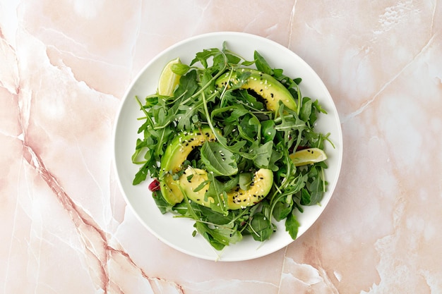 Ensalada verde fresca con aguacate y rúcula de lechuga mixta sobre plato blanco y fondo de mármol