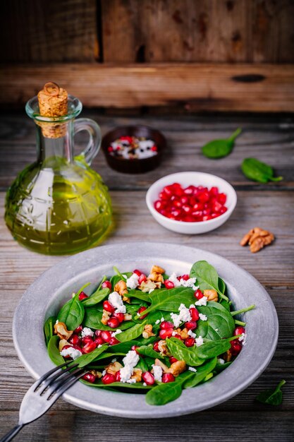 Ensalada verde fresca con espinacas, nueces, queso feta y granada sobre fondo de madera