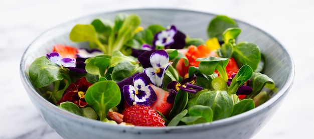Ensalada verde fresca con fresas y flores comestibles en un bol Fondo de mármol Cerrar