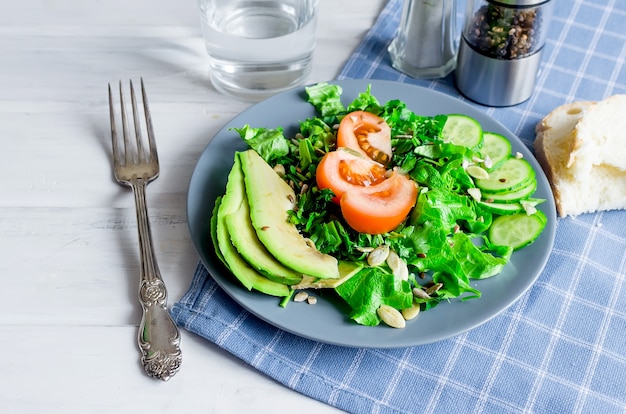 Ensalada verde fresca con pepino, lechuga, aguacate y tomates y vaso de agua