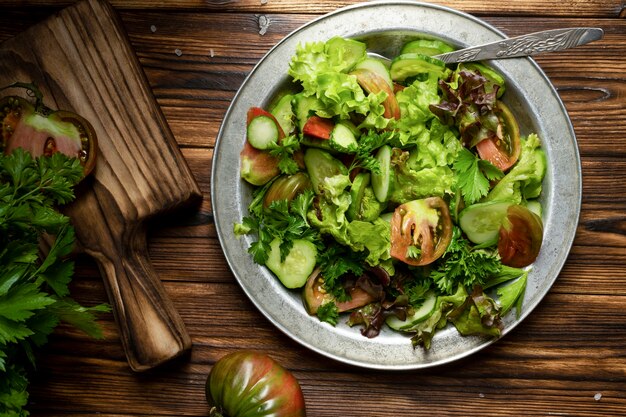 Ensalada verde fresca en recipiente de metal sobre mesa de madera. Estilo rústico.