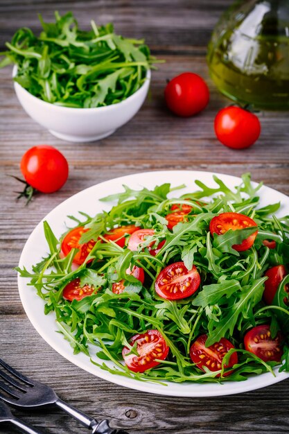 Ensalada verde fresca con rúcula y tomates rojos sobre fondo de madera rústica