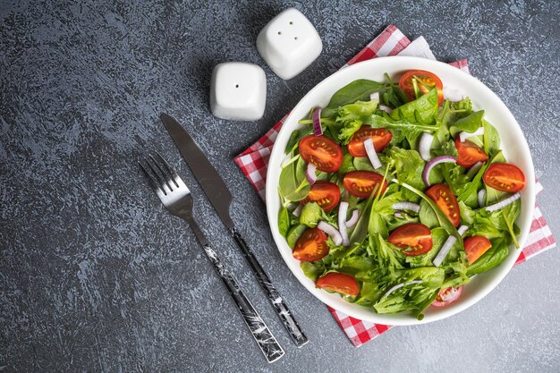 Ensalada verde de verano en plato blanco sobre mesa gris