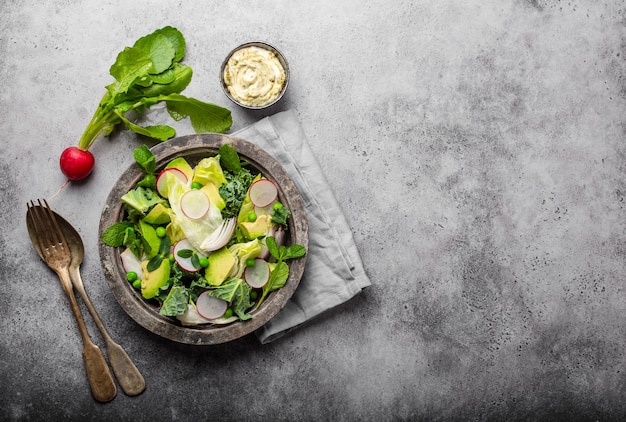 Ensalada de verduras con aguacate, col rizada, brotes de hierbas en un tazón rústico servido con salsa, fondo de hormigón gris, primer plano, vista superior. Alimentación sana y limpia, concepto de dieta / desintoxicación con espacio para texto