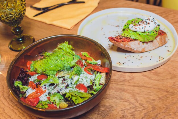 Ensalada de verduras con aguacate, pepino, tomate cherry, hojas de acelga y brócoli en un plato sobre la mesa de madera