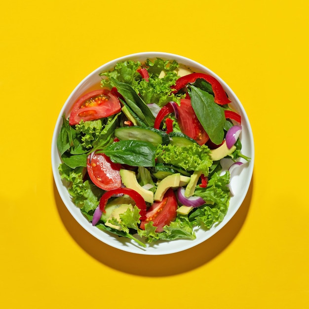 Ensalada de verduras con aguacate en un plato blanco sobre un fondo amarillo Dieta de cocina