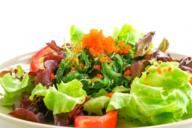 Ensalada de verduras con algas japonesas y huevos de camarones sobre fondo blanco.