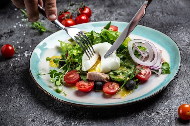 Ensalada de verduras con atún, poché, huevo, lechuga, cereza, tomate y aceitunas. Concepto de deliciosa comida equilibrada