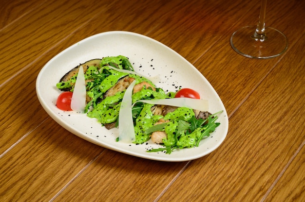 Ensalada de verduras con berenjena frita en un plato blanco sobre fondo de madera