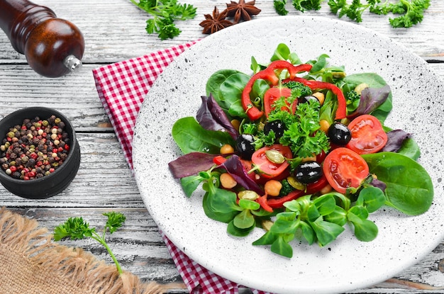 Ensalada de verduras con espinacas, tomates, pimentón y semillas de calabaza en un plato sobre un fondo de madera Vista superior Espacio libre para su texto Plano