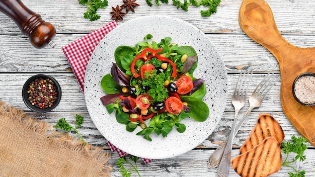 Ensalada de verduras con espinacas, tomates, pimentón y semillas de calabaza en un plato sobre un fondo de madera Vista superior Espacio libre para su texto Plano