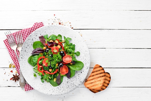 Ensalada de verduras con espinacas, tomates, pimentón y semillas de calabaza en un plato sobre un fondo de madera Vista superior Espacio libre para su texto Plano