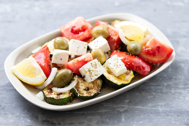 Ensalada de verduras frescas y asadas en un plato blanco sobre cerámica gris