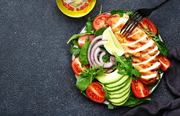 Ensalada de verduras frescas con filete de pollo a la parrilla tomates espinacas aguacate y cebolla roja con aceite de oliva sobre fondo negro Alimentos dietéticos cetogénicos de desintoxicación saludable Vista superior