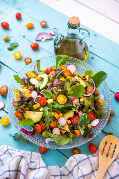 Ensalada de verduras frescas orgánicas y una botella de aceite de oliva virgen extra sobre un fondo azul.