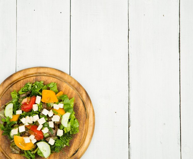 Ensalada de verduras frescas con queso verde tomates pepino sobre una mesa de madera blanca