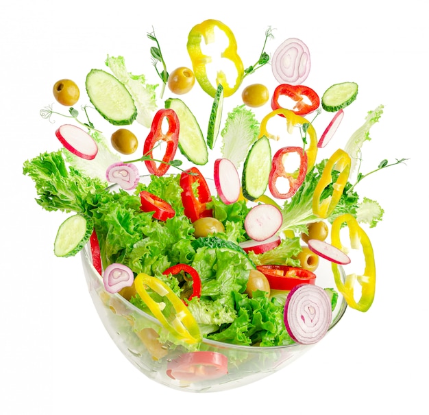 Ensalada de verduras frescas en un recipiente transparente con ingredientes voladores aislados en blanco. Nutrición apropiada.