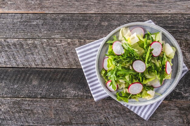 Ensalada de verduras frescas con rúcula de rábano y lechuga en un plato sobre fondo rústico con espacio de copia Vista superior