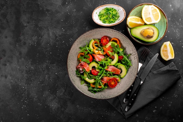 Ensalada de verduras frescas de verano con rúcula, tomates, pimientos, aguacate y salmón en una vista superior de la placa.