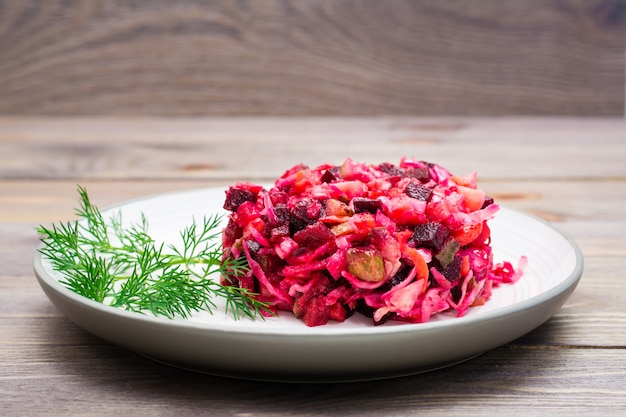 Ensalada de verduras hervidas, chucrut y pepinos en vinagre en un plato sobre una mesa de madera.