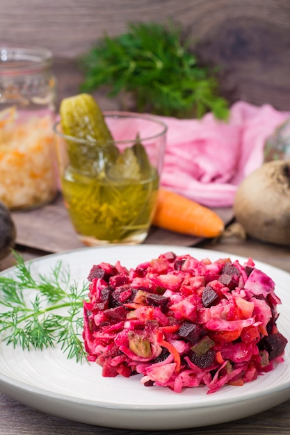 Foto ensalada de verduras hervidas, chucrut y pepinos en vinagre en un plato sobre una mesa de madera