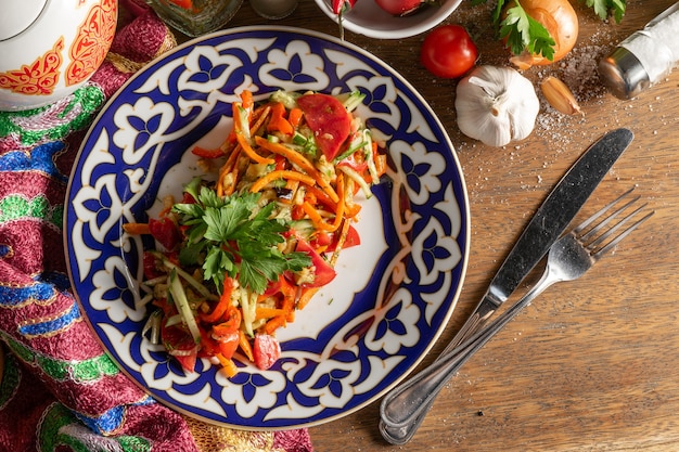 Ensalada de verduras Khorovats veganas de berenjenas al horno, tomates, zanahorias y pimientos en un plato con un patrón tradicional uzbeko