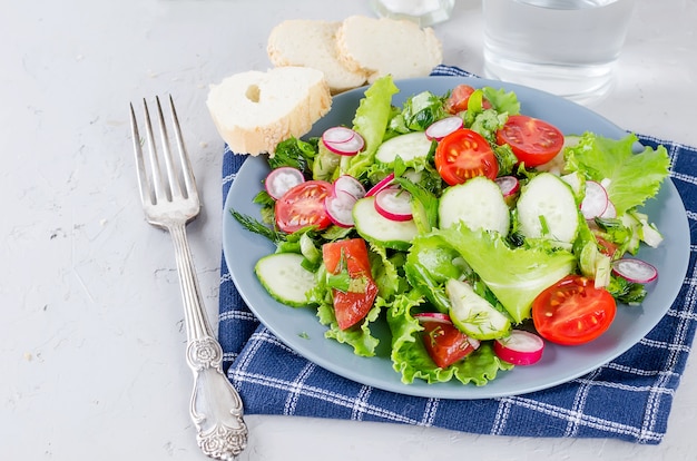 Ensalada de verduras de lechuga fresca, tomates, pepinos, rábanos y cebollas en la mesa.