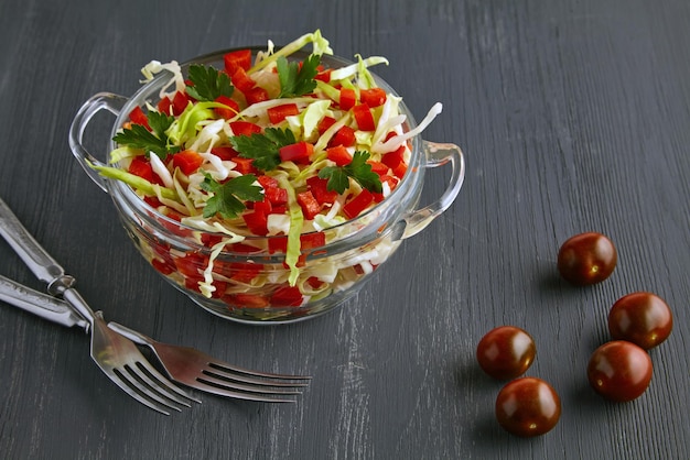 Ensalada de verduras ligera de col y pimientos en un cuenco de vidrio y cubiertos en una mesa de madera negra