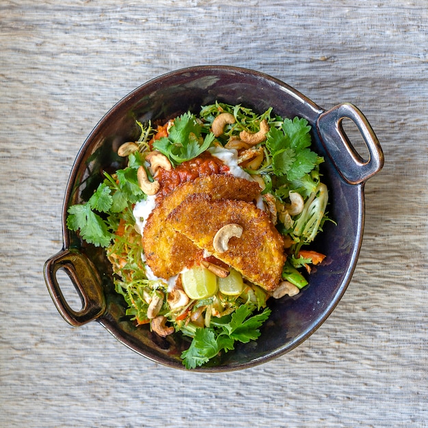 Ensalada de verduras orgánicas de brócoli, anacardos, chile suave y lima. Picante y vibrante con galanga y lima kaffir. Cubierto con buñuelos de maíz y una rica salsa de pimentón en la isla de Bali, Indonesia