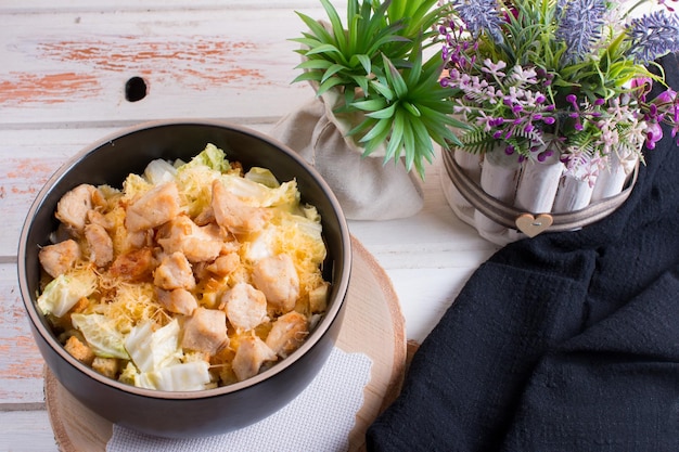 Ensalada de verduras con pechuga de pollo frita en un plato hondo Sirviendo sobre un fondo de madera con una servilleta negra y cubiertos