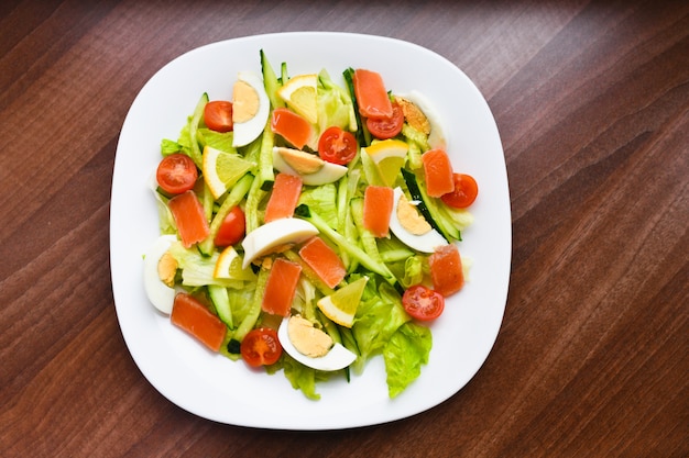 Ensalada de verduras en un plato blanco. Ensalada fresca con huevo, tomate, espinacas y aguacate en una superficie de madera blanca vista desde arriba. Comida sana.