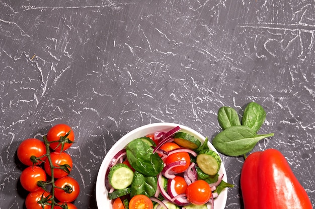 Ensalada de verduras en un plato blanco sobre un fondo gris