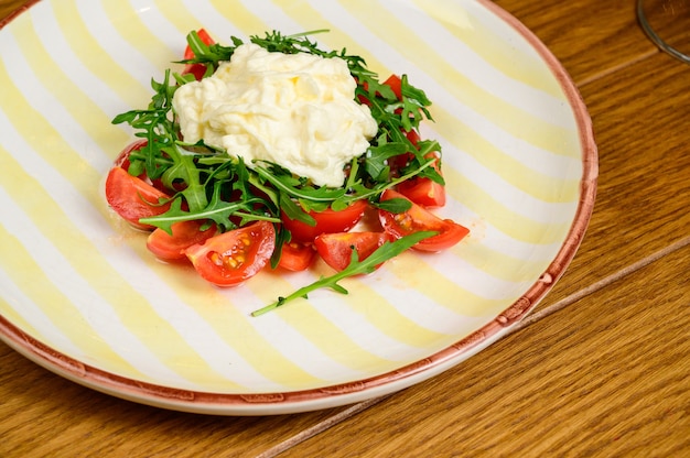 Ensalada de verduras de primavera con tomates en un plato blanco sobre fondo de madera