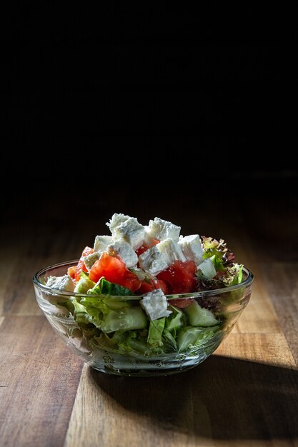 Ensalada de verduras con queso. Mesa de madera oscura