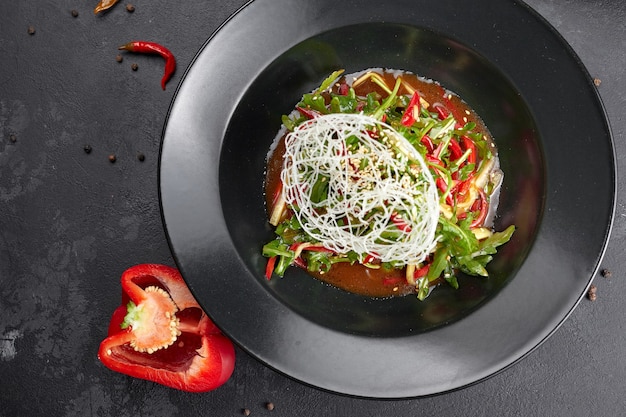 Ensalada de verduras con rúcula, pimiento, pepino y semillas de lino, sobre un fondo negro