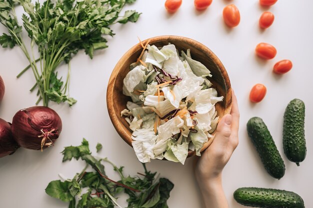 Ensalada de verduras saludables en un cuenco de madera con ingredientes sobre una mesa blanca