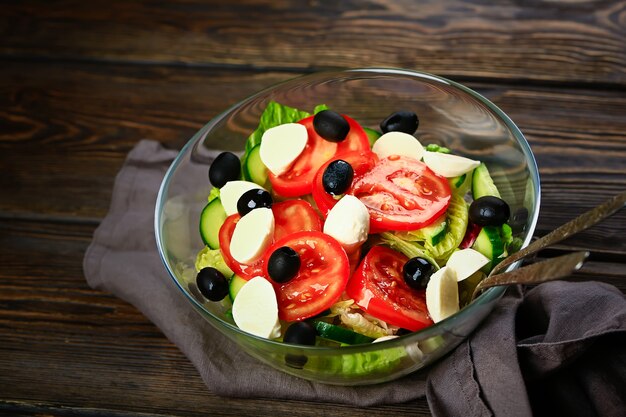 Ensalada de verduras sobre un fondo de madera. Lechuga, tomate, pepino, aceitunas, mozzarella y aceite de oliva. Comida sana y saludable.