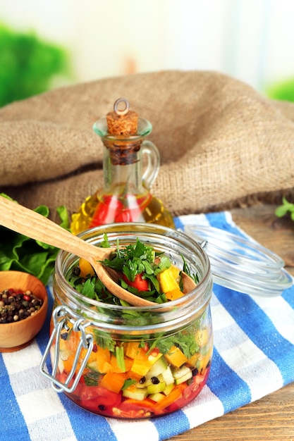 Ensalada de verduras en tarro de cristal en servilleta sobre fondo de madera