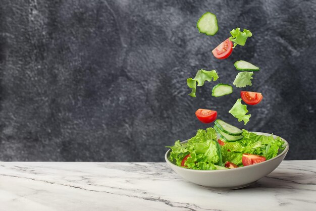 ensalada de verduras verdes frescas que caen en un plato sobre un fondo gris