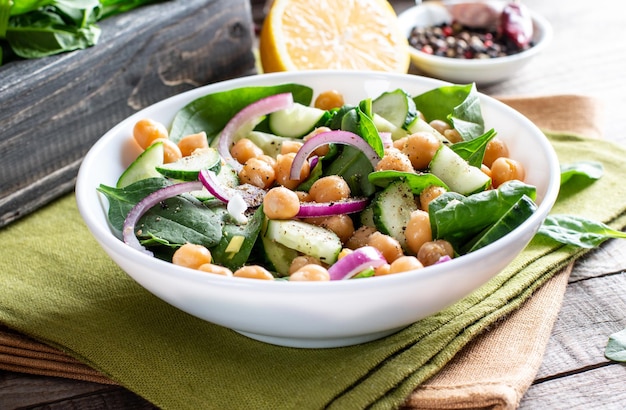 Ensalada de verduras verdes con garbanzos, espinacas, pepino, cebolla roja y verduras sobre un fondo claro de pizarra, piedra u hormigón.