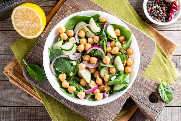 Ensalada de verduras verdes con garbanzos, espinacas, pepinos, cebollas rojas y verduras en una mesa de madera