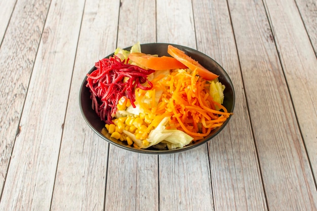 Ensalada de verduras con zanahoria de maíz dulce y ralladura de remolacha roja tomates cortados en cubitos y lechuga iceberg en un tazón negro