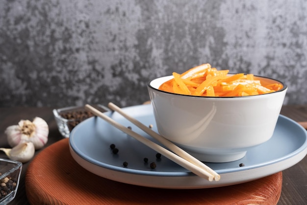 Ensalada de zanahoria coreana con salsa picante y picante en una ensaladera blanca contra una pared de hormigón