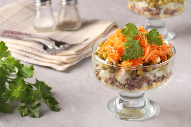 Ensalada con zanahorias coreanas, carne y guisantes enlatados en una ensaladera transparente una superficie gris claro, espacio de copia